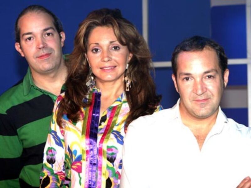 Tres personas posando juntas en un entorno de estudio con un fondo azul y blanco.