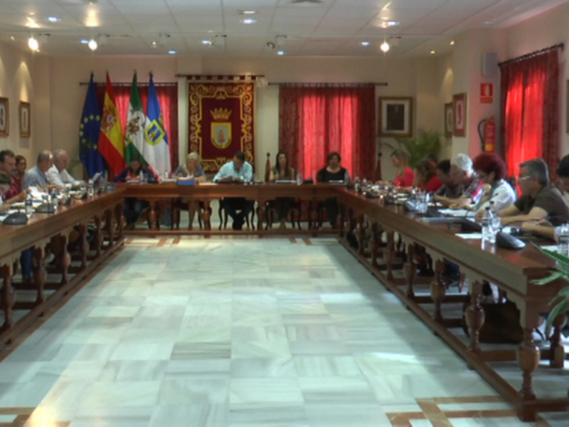Reunión de trabajo en una sala de conferencias con banderas y escudos de España y Andalucía en el fondo.