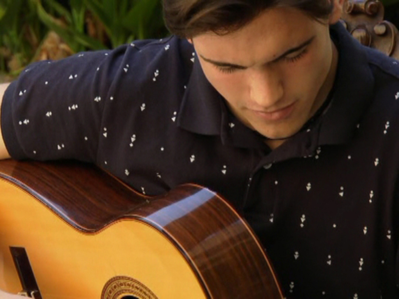 Joven tocando una guitarra acústica en un entorno natural con vegetación en el fondo.