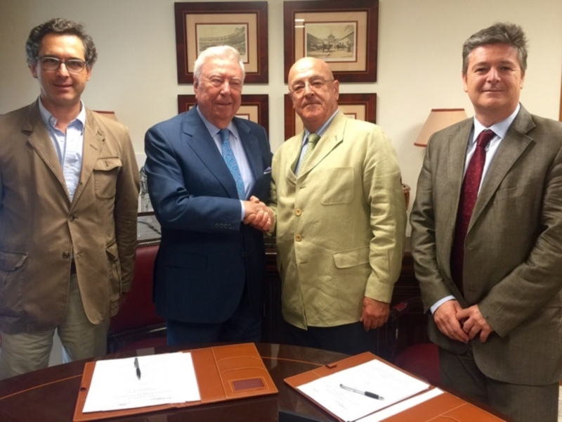 Tres hombres en trajes posan para una foto en una oficina, con documentos y bolígrafos en la mesa.