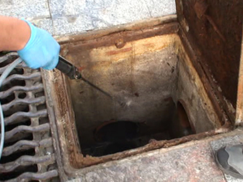 Un trabajador con guantes azules inspecciona una alcantarilla con un cable de inspección, mostrando la necesidad de mantenimiento y seguridad en las labores de mantenimiento de alcantarillas.