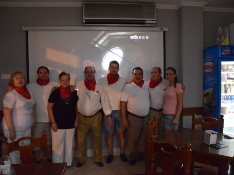 Grupo de personas posando en una reunión, todos con bufandas rojas, frente a una proyección de la marca 'etb'.