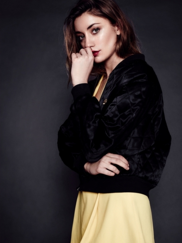Moda: mujer con chaqueta bomber negra y falda amarilla, fondo oscuro.
