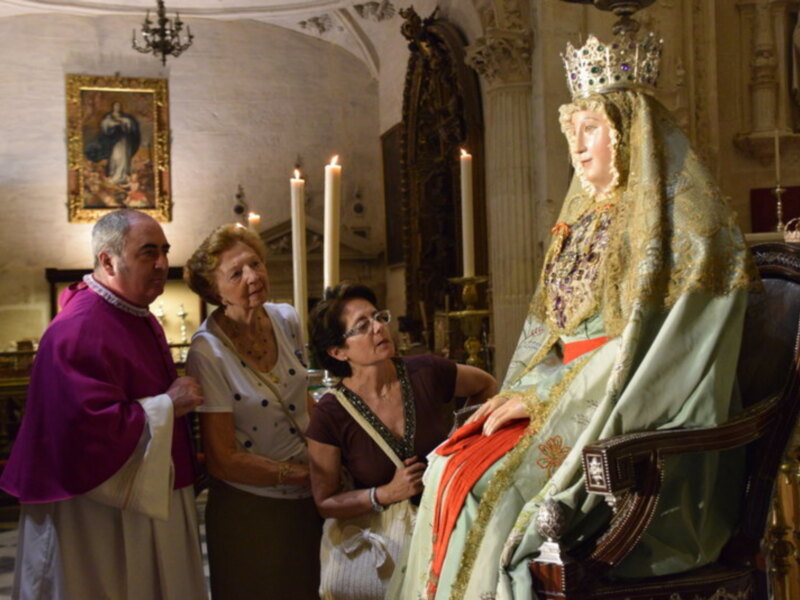 Celebración religiosa con la imagen de la Virgen en un santuario, rodeada por fieles y un sacerdote.
