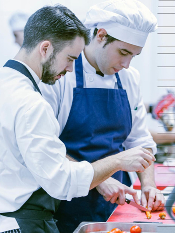 Dos chefs en uniforme azul y blanco cortan verduras en un mostrador de cocina.