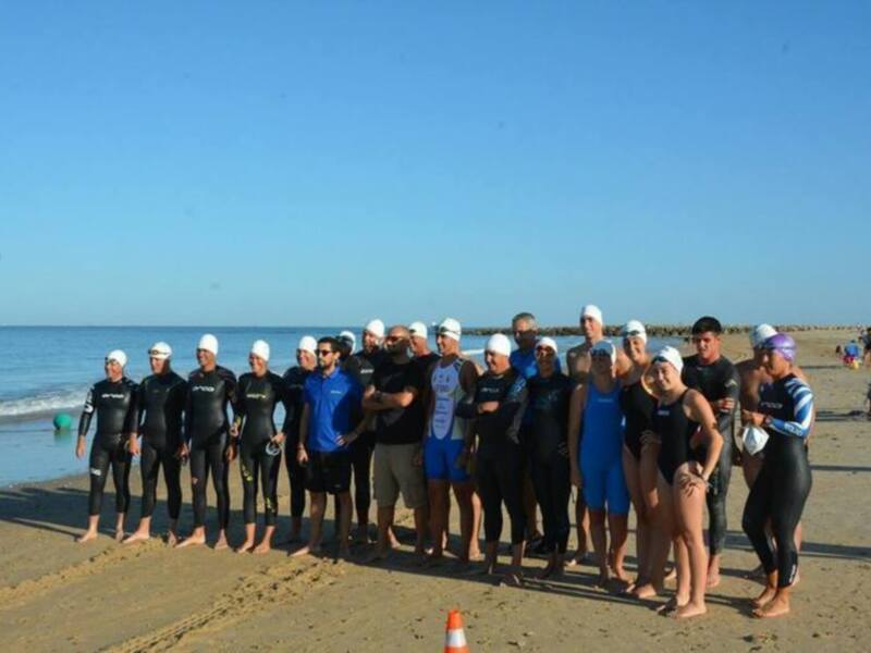 Equipo de nadadores en traje de baño y gorras posando en la playa antes del evento.