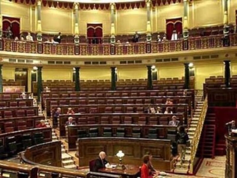Salón de sesiones del Parlamento de Australia, con bancas rojas y columnas verdes en el fondo.
