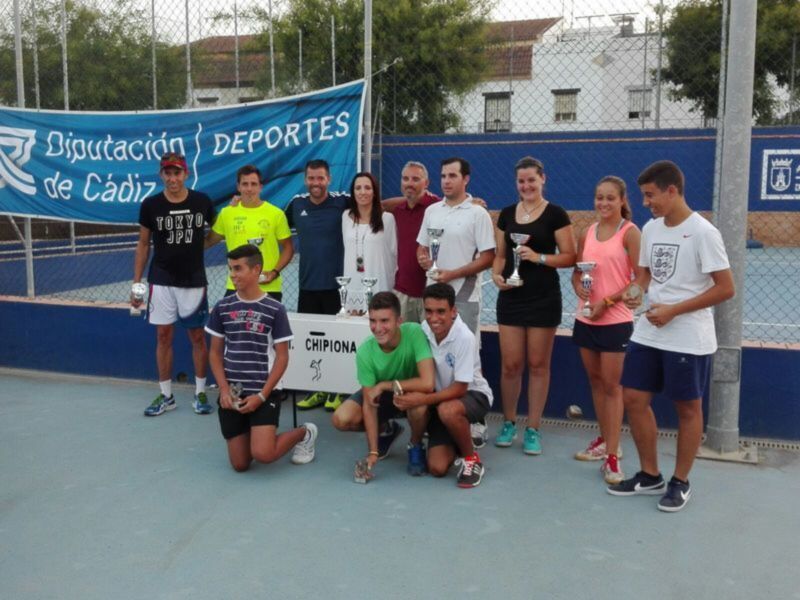Equipo de tenis posando con trofeos en una cancha deportiva.
