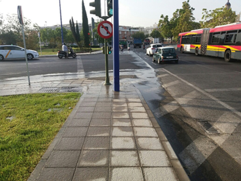Calle mojada con señal de prohibido girar a la izquierda y vehículos en movimiento.