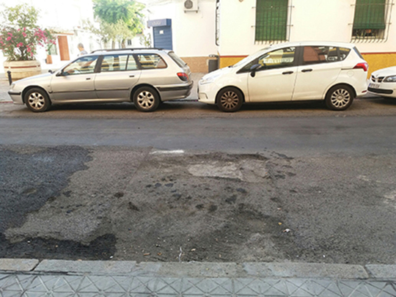 Vehículos estacionados en una calle con un agujero profundo en el asfalto. El agujero parece ser una zona de reparación o mantenimiento en la carretera.