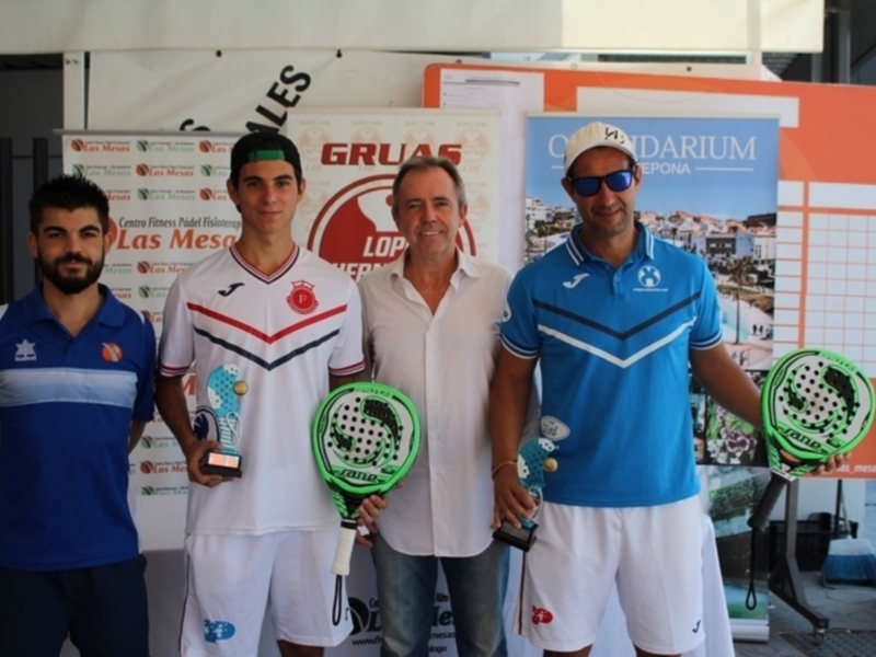 Equipo de padel posando con sus raquetas y trofeo en un evento deportivo.
