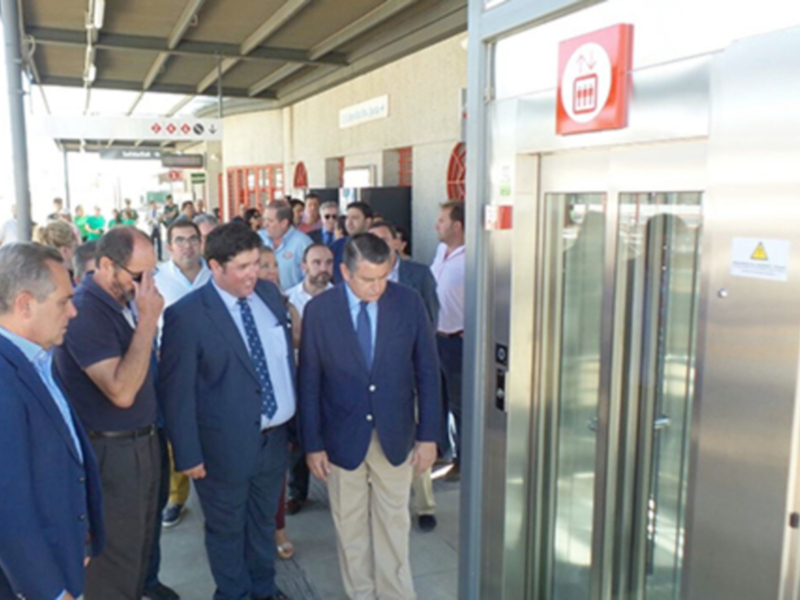 Gente esperando en una estación de metro o tren, con una señal de emergencia visible en el fondo.