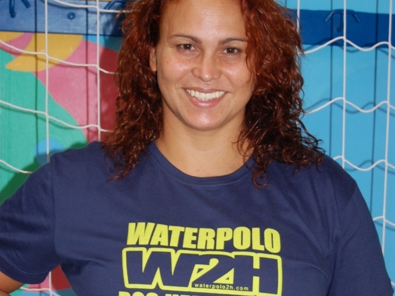 Una mujer con cabello rojo y una camiseta azul con letras amarillas y azules que dice 'Waterpolo 2h'.