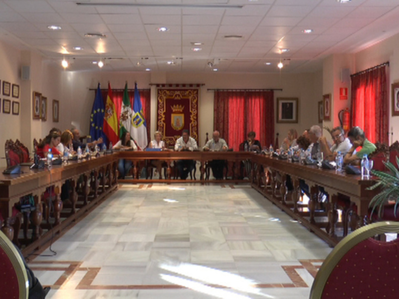 Reunión en una sala de conferencias con banderas y un escudo en el fondo.