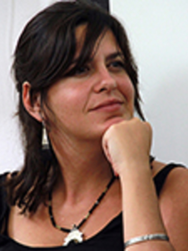 Una mujer con cabello oscuro y una sonrisa suave, con una mano levantada alrededor de su mejilla, posando con una expresión pensativa y relajada.