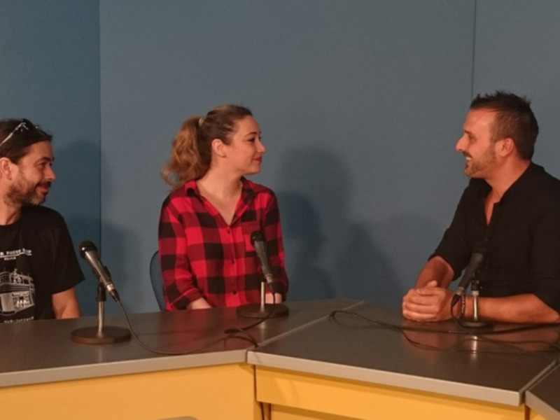 Tres personas sentadas en una mesa con micrófonos, posiblemente en una conferencia o evento.