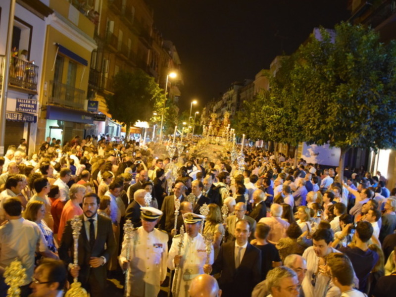 Procesión nocturna en Sevilla con multitud de personas y figuras religiosas procesionales.