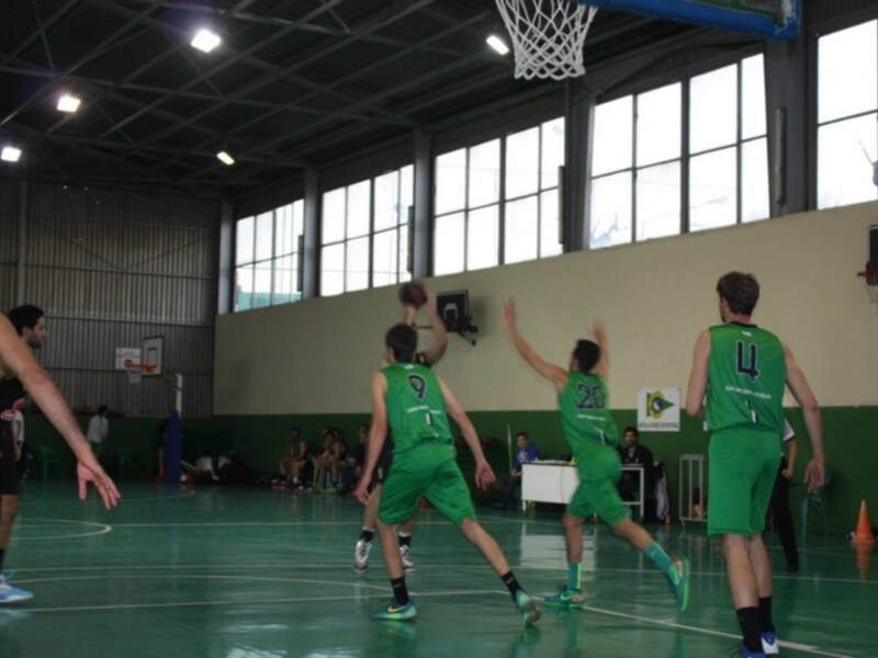 Jugadores en un partido de baloncesto en una cancha deportiva, con equipo verde en acción.