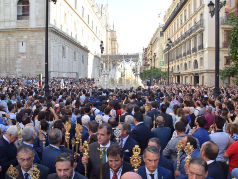 Una multitud de personas en una procesión religiosa, con palmas y vestidos formales, frente a un edificio histórico.