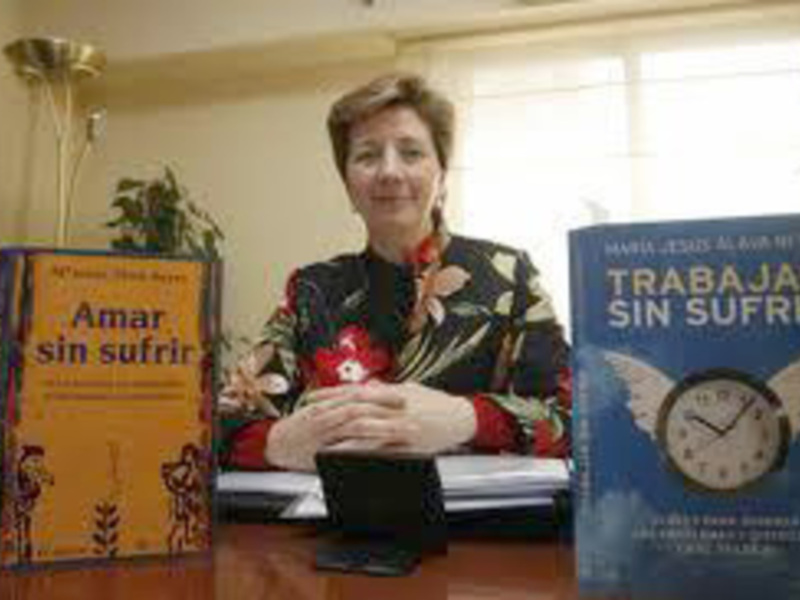 Mujer sentada detrás de una mesa con libros titulados 'Amar sin sufrir' y 'Trabajar sin sufrir'.
