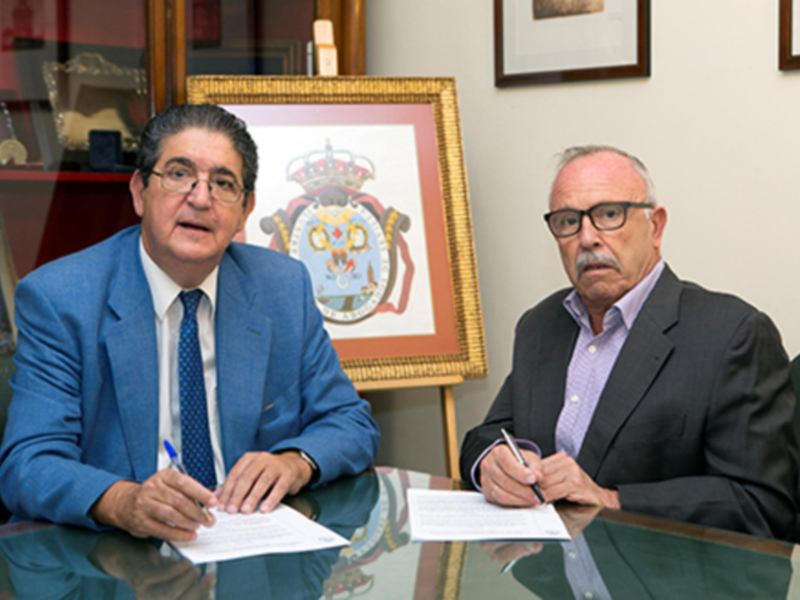 Dos hombres sentados en una oficina, uno con un documento en la mano, posiblemente firmando un acuerdo.