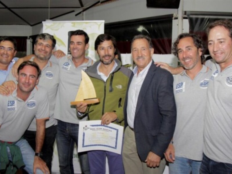 Equipo de personas en una reunión, con un hombre sosteniendo un trofeo y un documento, posiblemente en un evento deportivo o empresarial.