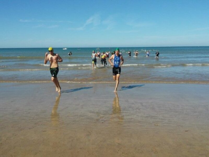 Atletas corriendo en la playa durante una competencia de triatlón.