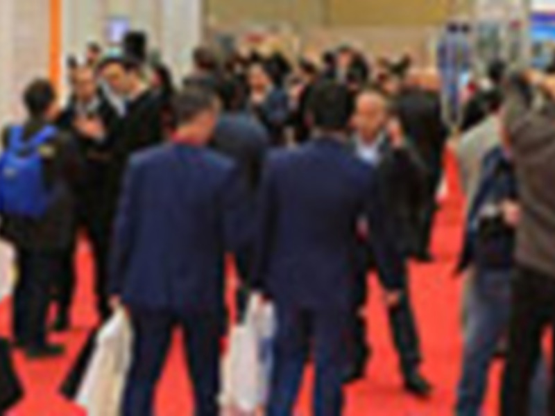 Una gran cantidad de personas en una feria o evento, con stands y stands en el fondo, mostrando un ambiente de negocios y networking.