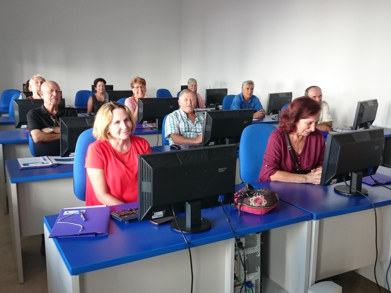 Grupo de adultos mayores participando en una clase de informática en un aula bien iluminada.