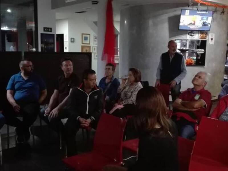 Grupo de personas reunidos en una sala de reuniones, escuchando una presentación en pantalla.