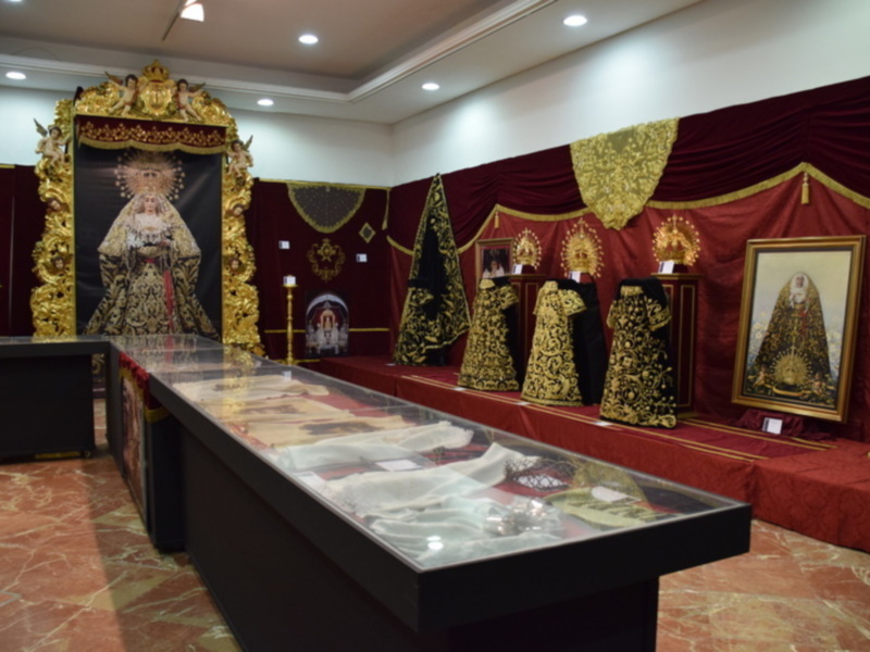 Una sala de exposición con vitrinas y telas bordadas en dorado y negro, posiblemente en un museo religioso o cultural.