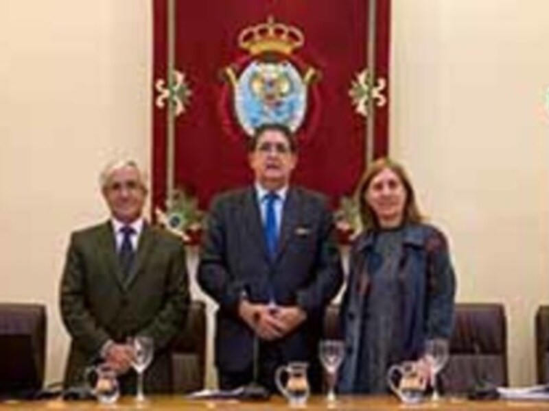 Tres personas en una reunión, con una bandera española y un logotipo de la Universidad de Alcalá de Henares en el fondo.