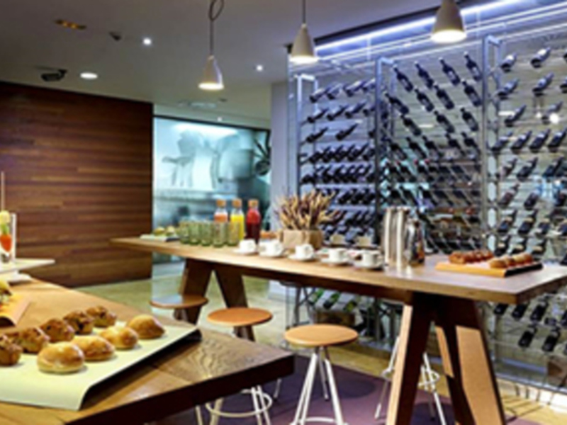 Interior de un restaurante moderno con mesa de desayuno, botelleros de vino y decoración minimalista.