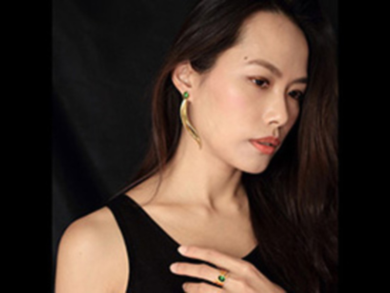 Elegante mujer con joyas de diseño moderno, destacando un anillo y pendientes curvos en un fondo oscuro.