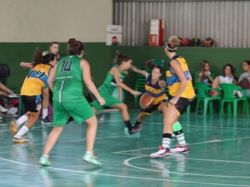 Partido de baloncesto femenino en cancha de interior, con jugadoras de equipos en verde y azul en acción.