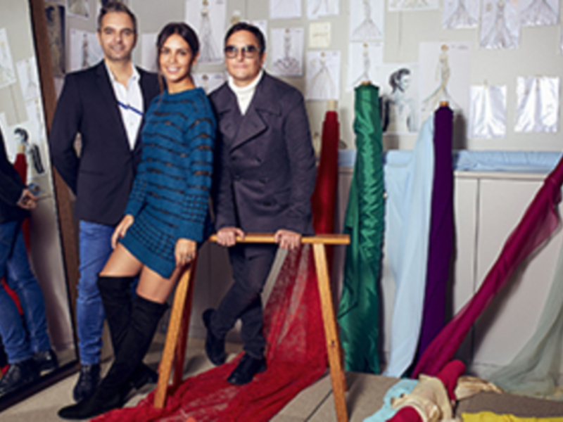 Tres personas posando en un estudio de diseño de moda con telas y bocetos en el fondo.