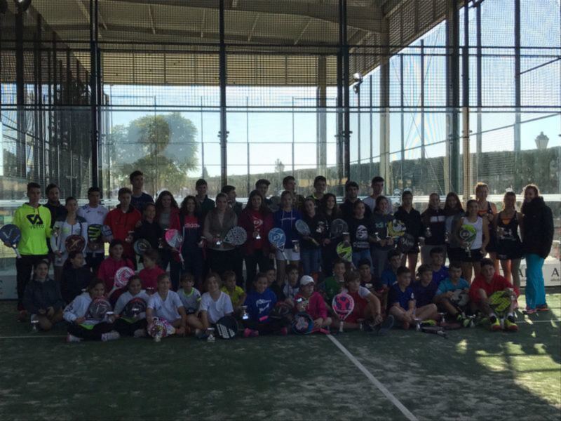 Gente en una cancha de pádel con raquetas de pádel en las manos, posando para una foto grupal.