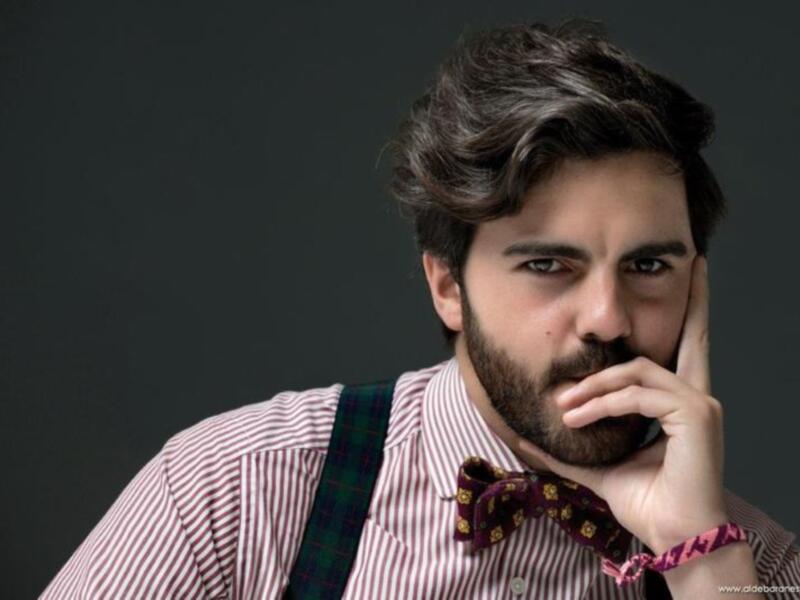 Hombre con camisa a rayas, corbata de pajarita y corbata de pañuelo, fondo oscuro.