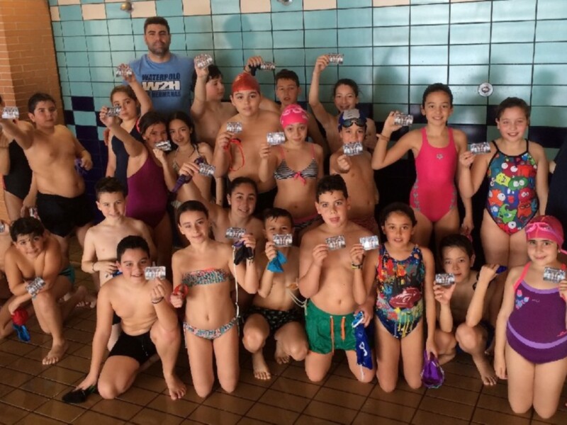 Grupo de niños y niñas en una piscina celebrando con botellas de agua.