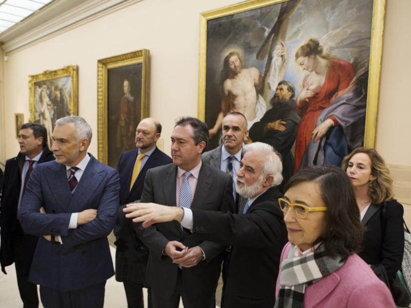 Una reunión formal en un museo, con personas en trajes y una pintura histórica en el fondo.
