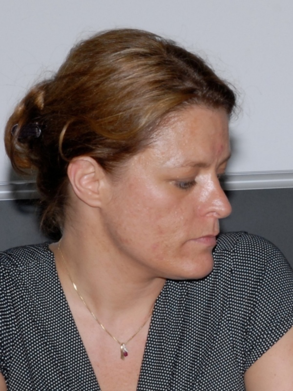 Mujer con cabello castaño recogido, vistiendo una blusa con lunares y una cadena de oro con colgante.
