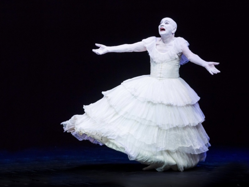 Una bailarina en un vestido blanco con volantes, realizando una pose con las manos extendidas hacia el cielo.