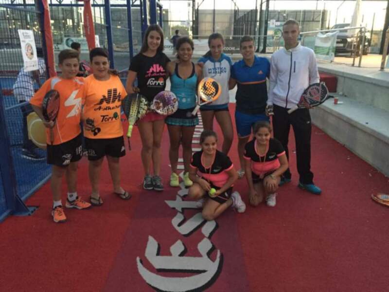 Grupo de personas posando para una foto en una cancha de pádel, con raquetas de pádel en la mano.