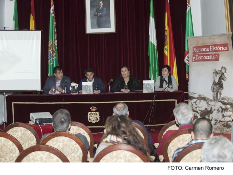 Conferencia sobre Memoria Histórica en un salón con banderas y carteles.