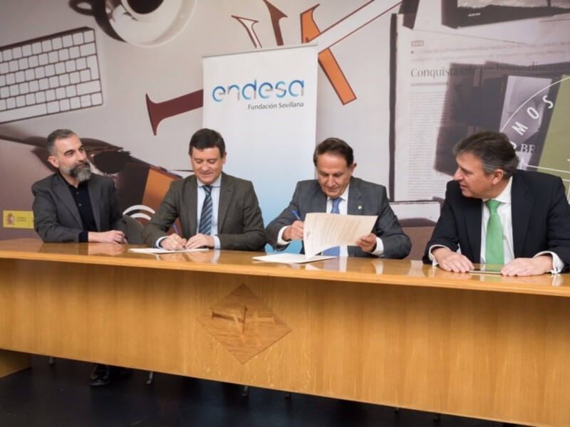 Tres hombres en trajes sentados en una mesa, firmando documentos en un evento de Fundación Sevillana. Detalle de la imagen: un banner con el logo de Endesa en el fondo. El evento parece ser un acuerdo o firma importante.