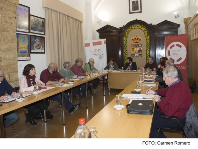 Reunión de trabajo en un salón con carteles de Cádiz y participantes anotando en documentos.