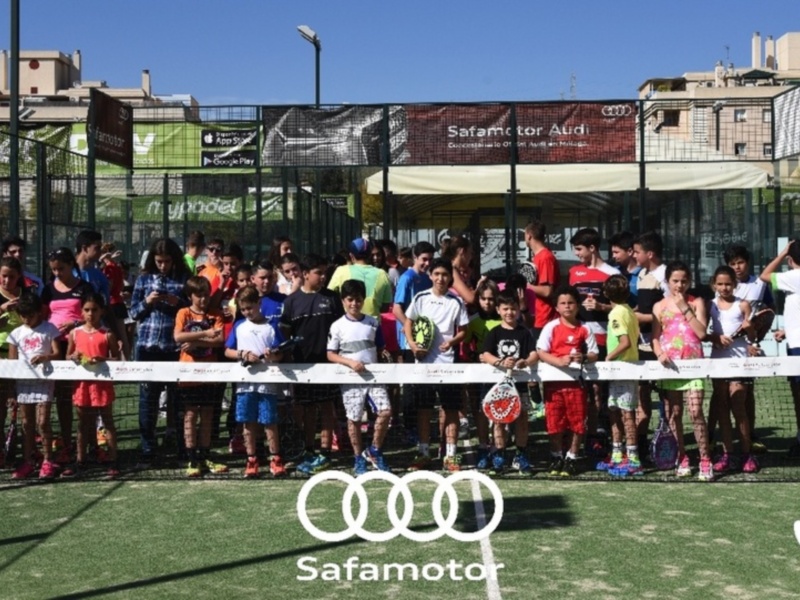 Niños y jóvenes participando en un torneo de pádel en un campo de césped, con un marco de seguridad y publicidad de Audi y Safamotor.
