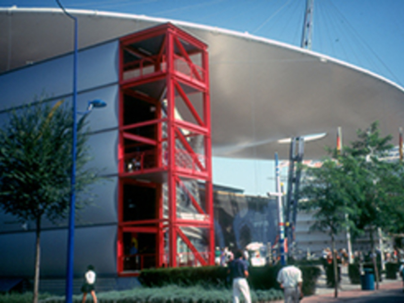 Escalera roja al exterior de un edificio moderno con estructura curva y árboles alrededor.