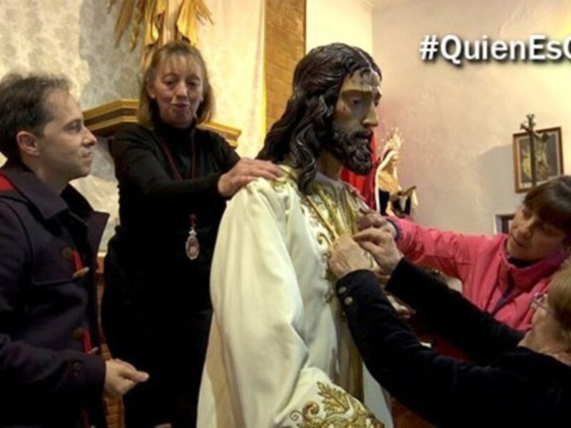 Personas adorando y ataviando una figura de Jesús en un entorno religioso.