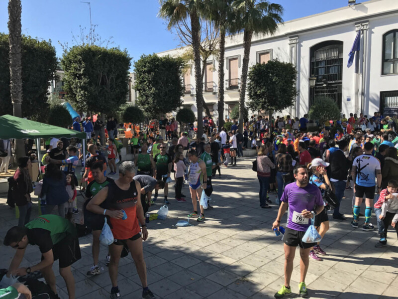 Atleta con número 767 participando en una carrera de atletismo en una plaza con árboles y edificios al fondo.